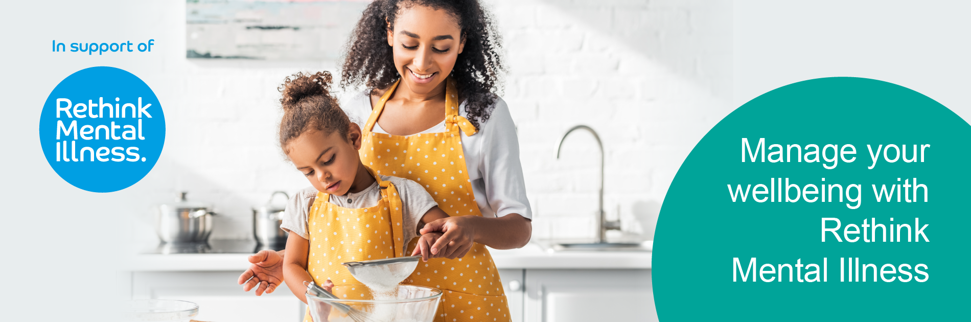 Female adult standing behind female child at table, both holding a sieve over a mixing bowl.